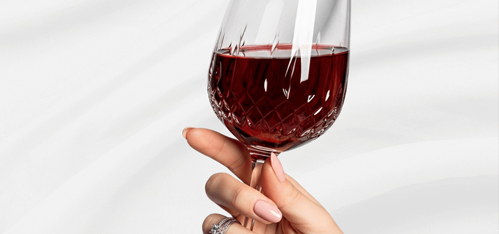 A hand with manicured nails holding a wine glass, set against a white background.